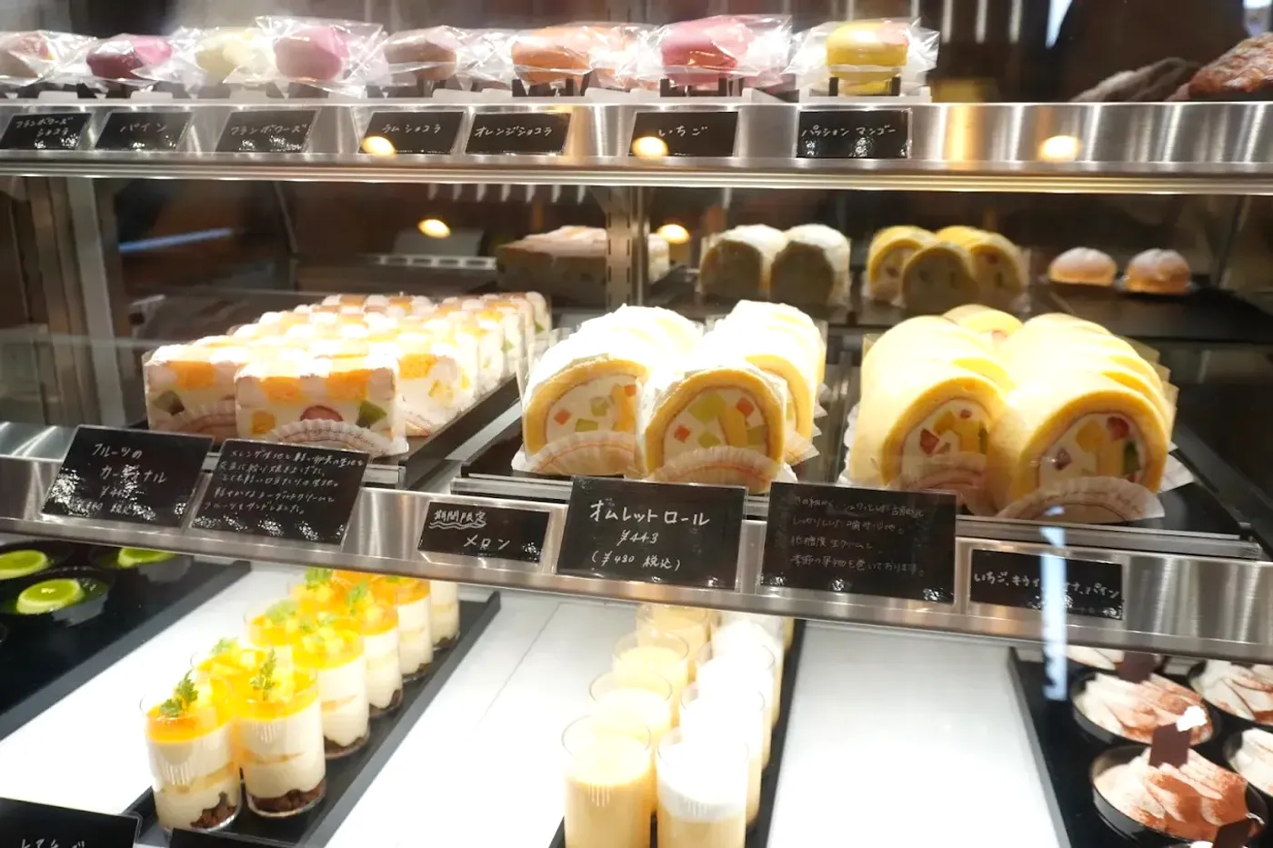 ショーケースに並ぶマカロン、ロールケーキ、ヴェリーヌと手書きの黒板カード